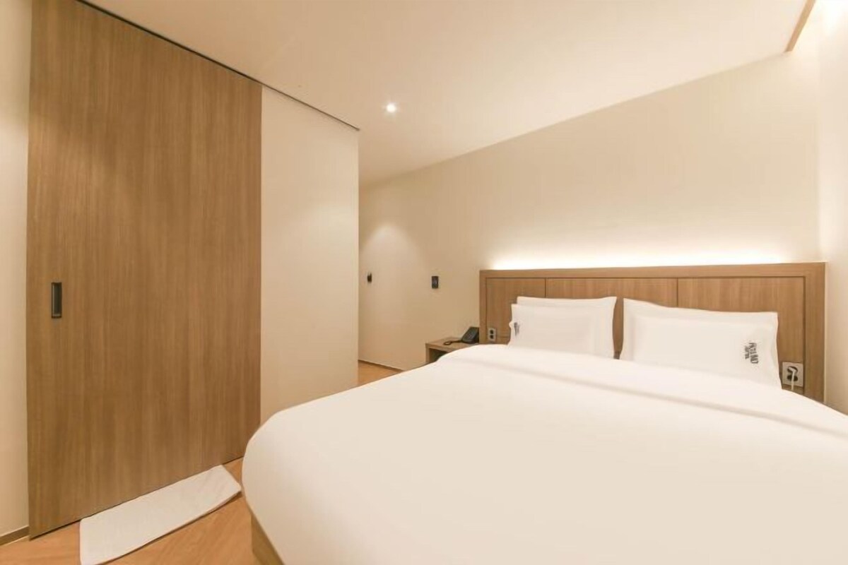Habitación de hotel moderna con una cama grande, armario de madera y mesita de noche con teléfono.