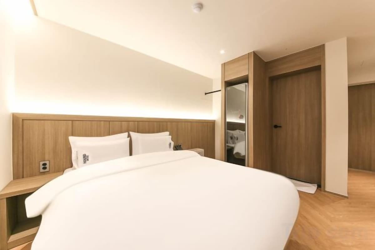 Habitación de hotel moderna con una cama grande, cabecera de madera, mesitas de noche y vestidor.