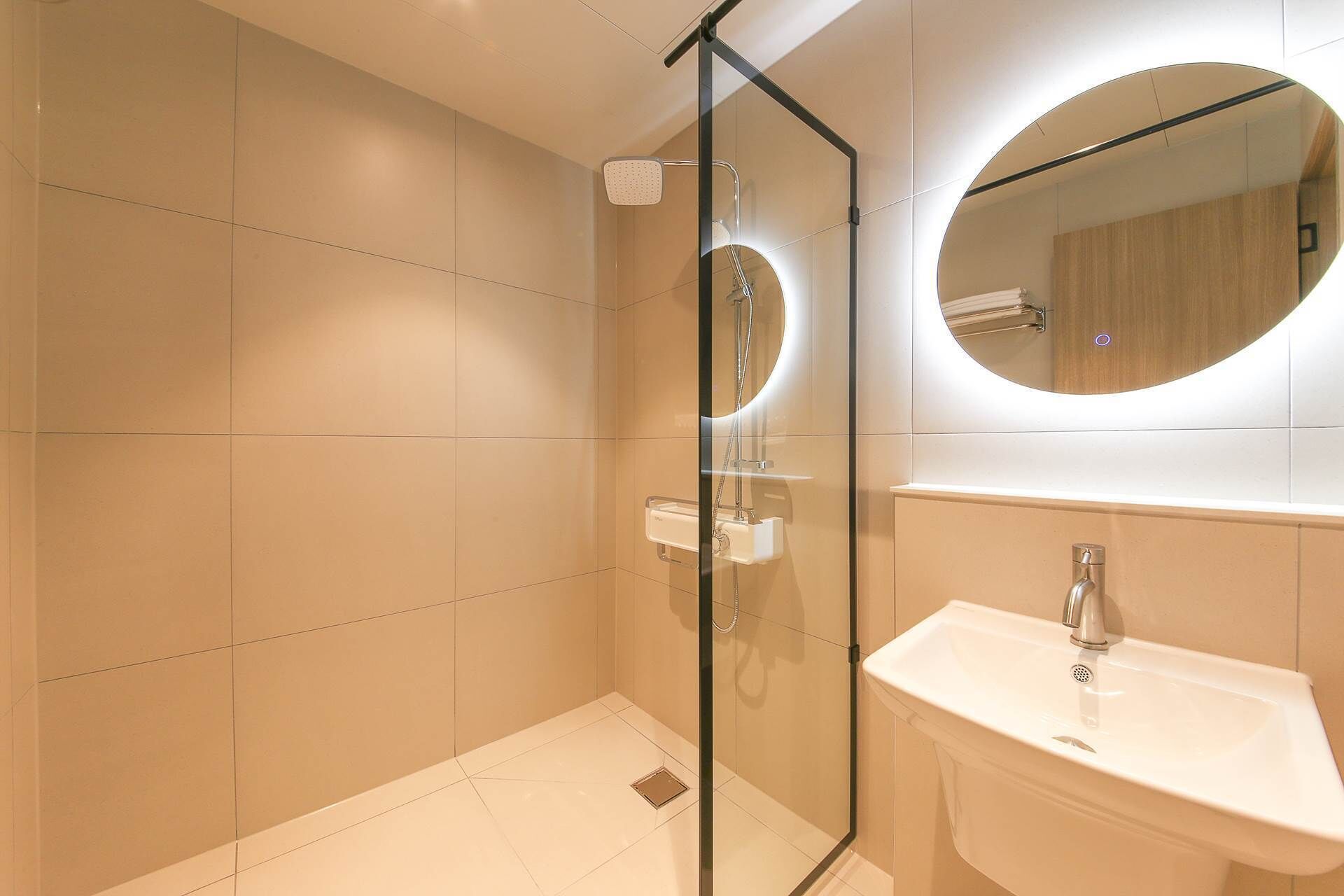 A modern bathroom with a glass-enclosed shower, a round mirror, and a white sink.