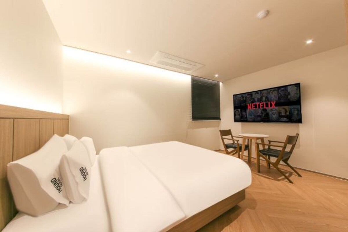 A modern hotel room with a bed, a TV mounted on the wall, and a small table with chairs.