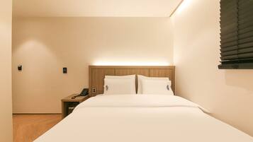 A hotel room with a large bed, a bedside table with a phone, and a wall-mounted light fixture.