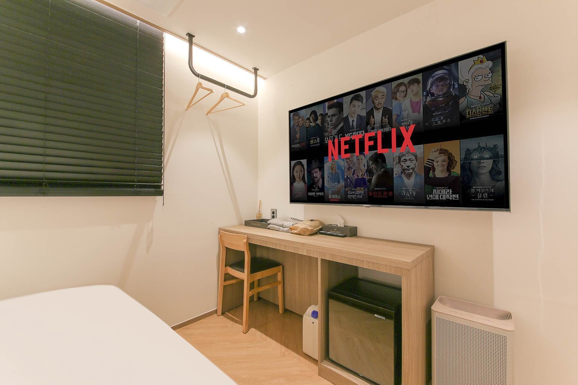 A small, modern room with a bed, a desk, and a wall-mounted TV displaying Netflix content.