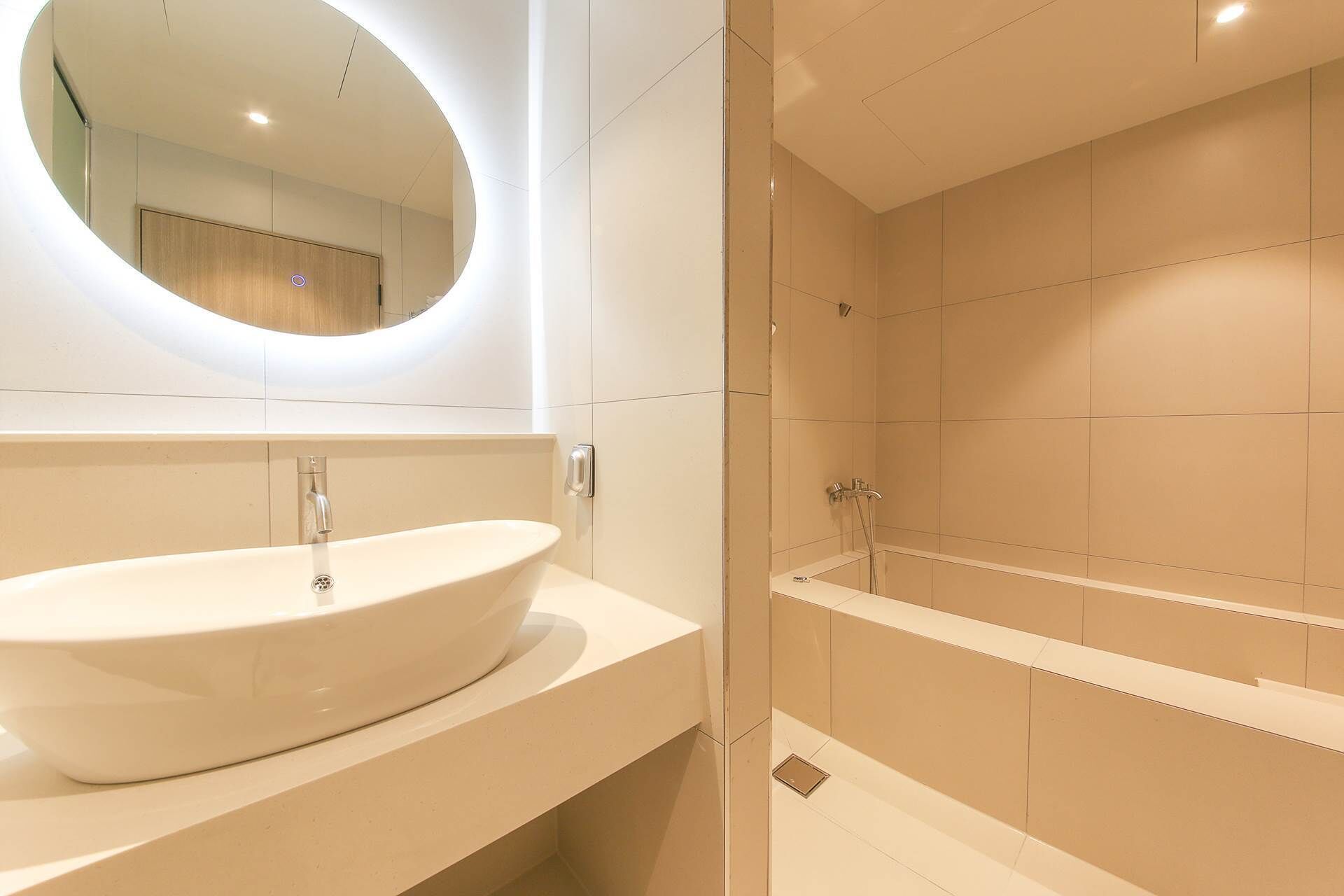 Een moderne badkamer met een groot ovaal wastafel, een spiegel en een afzonderlijke douche.