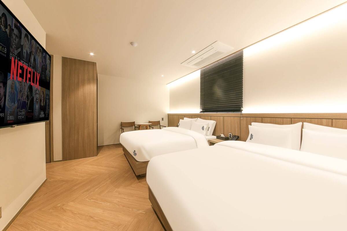 Habitación de hotel con dos camas, un televisor montado en la pared y piso de madera.