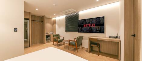 A modern hotel room with a large bed, a desk, two chairs, a TV mounted on the wall, and a wardrobe.