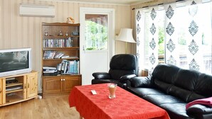 Een woonkamer met een houten tv-meubel, een zwarte leren bank, een rode tafel en een boekenplank.