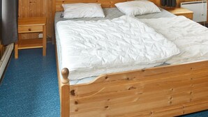 Een houten bed met witte beddengoed in een kamer met houten wanden en een blauw vloerkleed.
