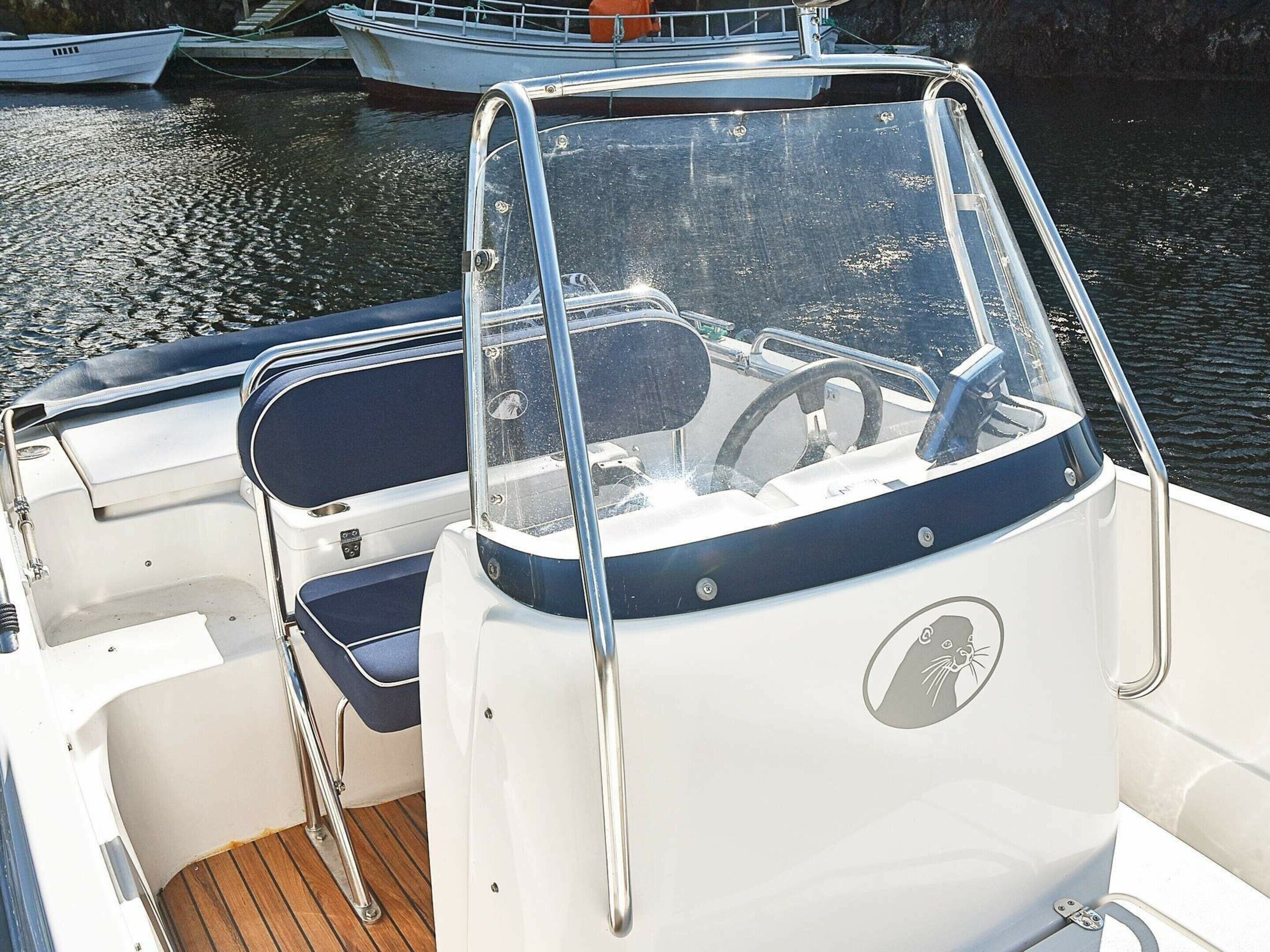 Interior de un barco con timón, asiento acolchado y barandilla metálica.