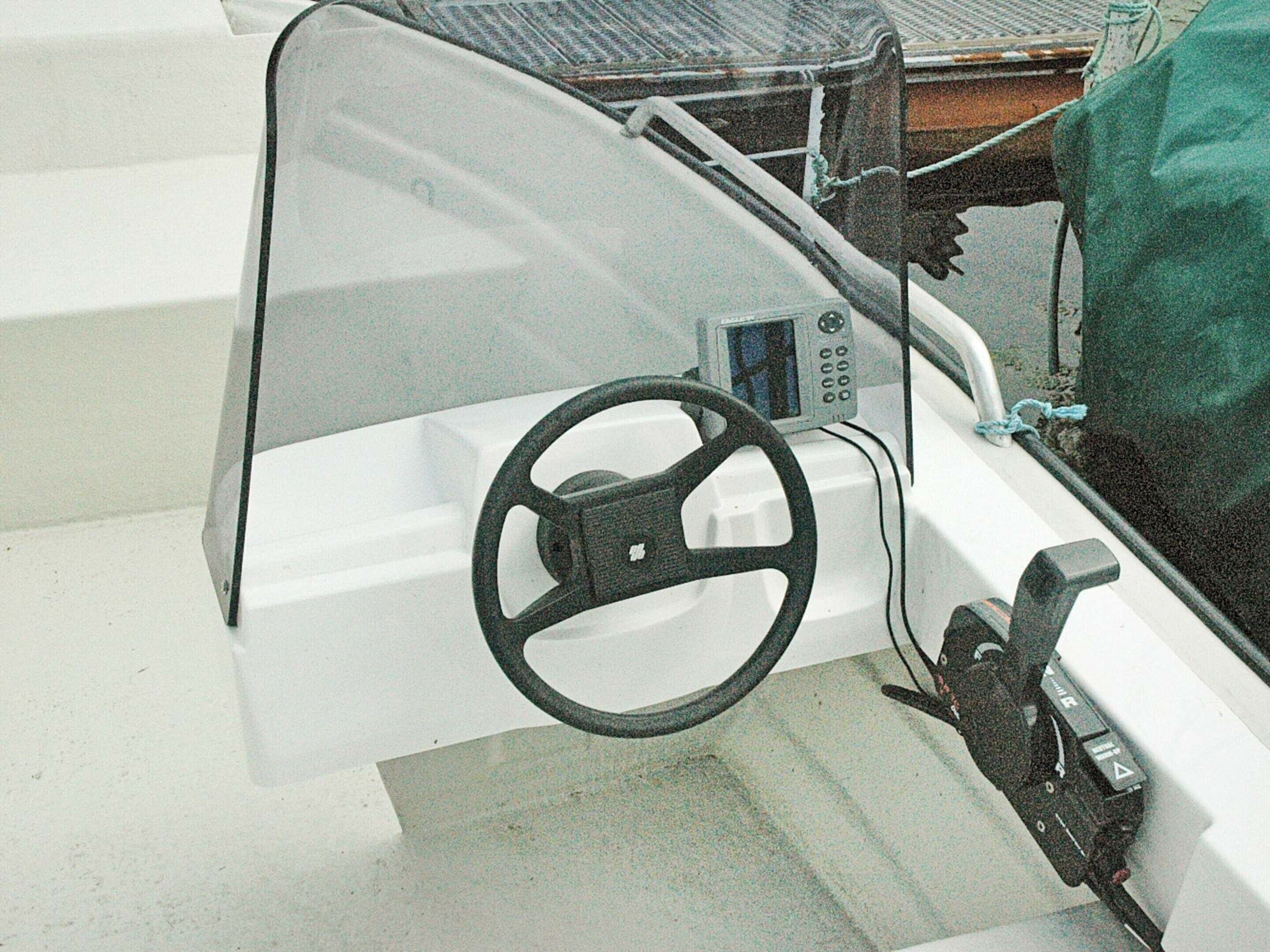 A boat's interior with a steering wheel, a control panel, and a green cover on the side.