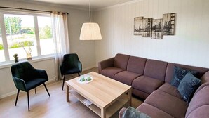 Un salon moderne avec un canapé marron, deux fauteuils noirs, une table basse en bois et une lampe suspendue.