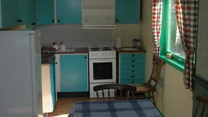 Cocina compacta con gabinetes color turquesa, una estufa blanca y una ventana con cortinas de cuadros.