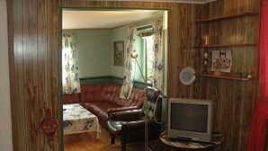 Una habitación con piso de madera, un sofá de cuero marrón, una mesita con un televisor y una pared con un reloj y marcos de fotos.