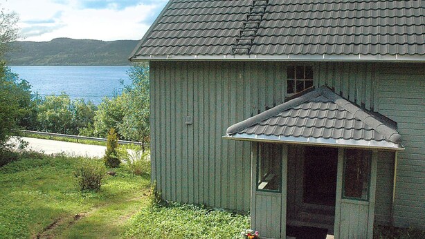 Una casa de madera con techo de tejas, un porche y vistas a un lago.