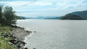Un lago tranquilo con orilla rocosa y montañas distantes bajo un cielo nublado.