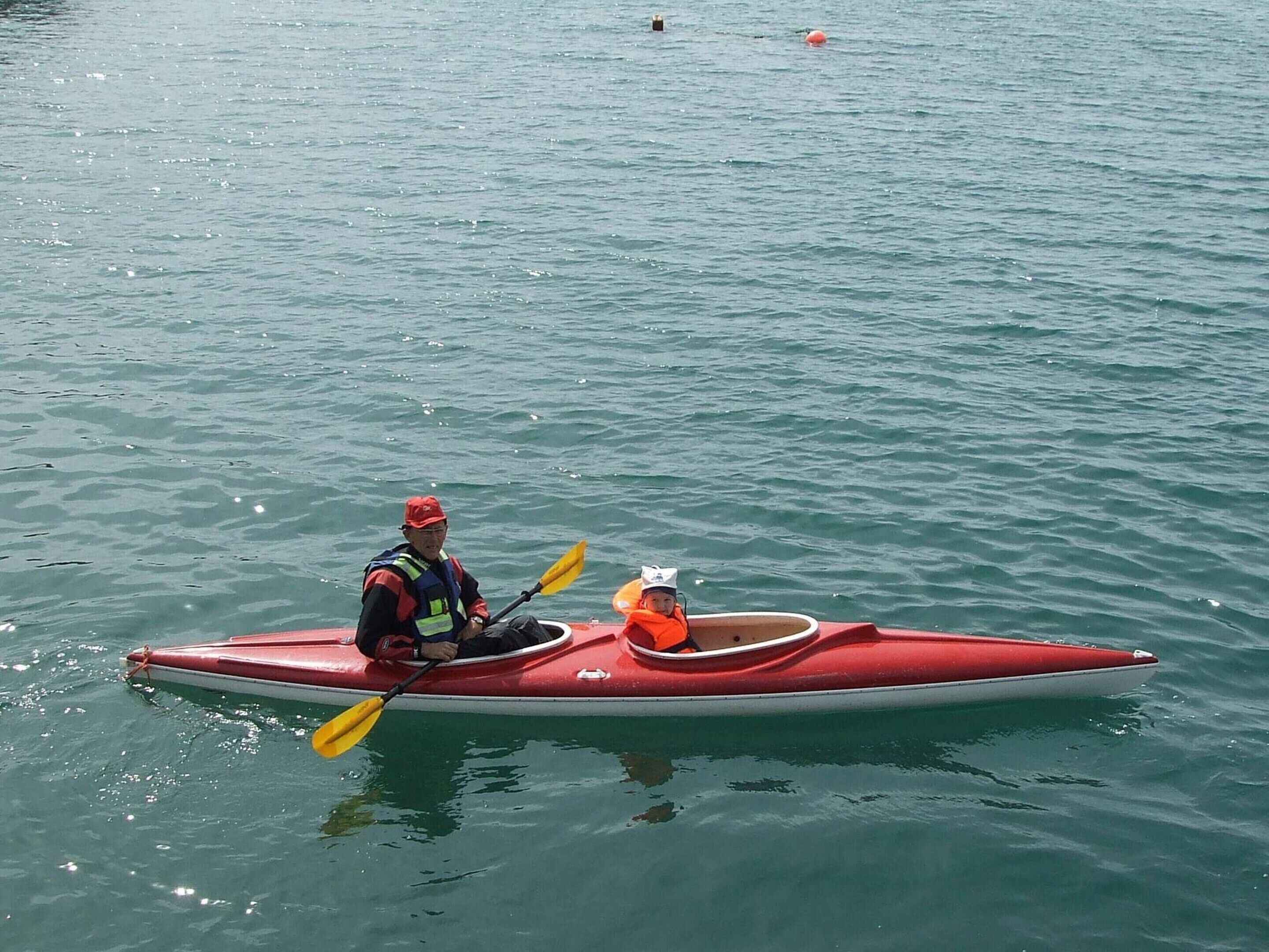 Eine Person paddelt in einem roten Kajak auf ruhigem Wasser.