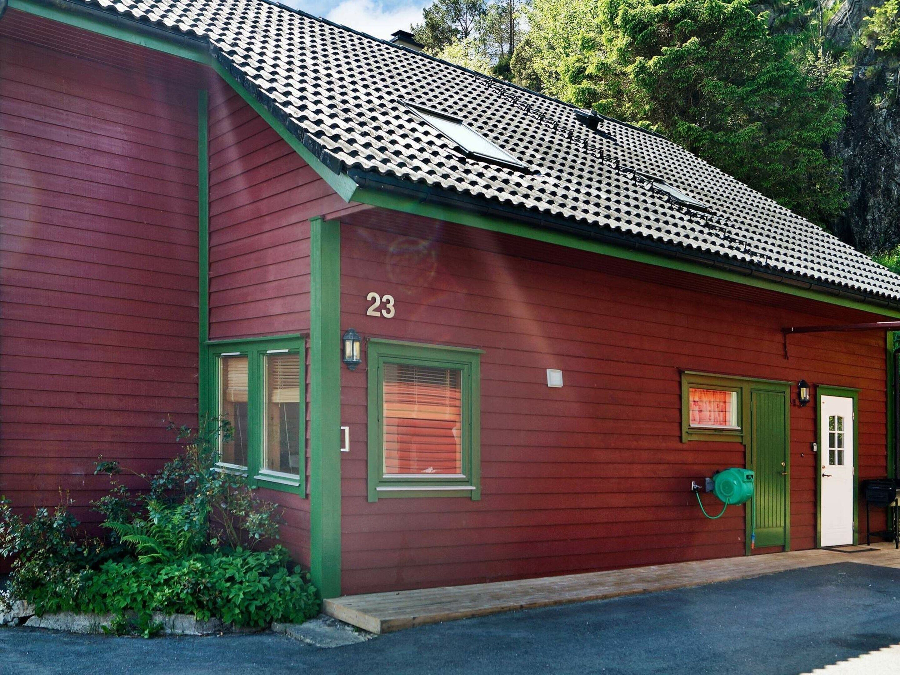 A red building with green trim, numbered 23, featuring a tiled roof and a small porch area.