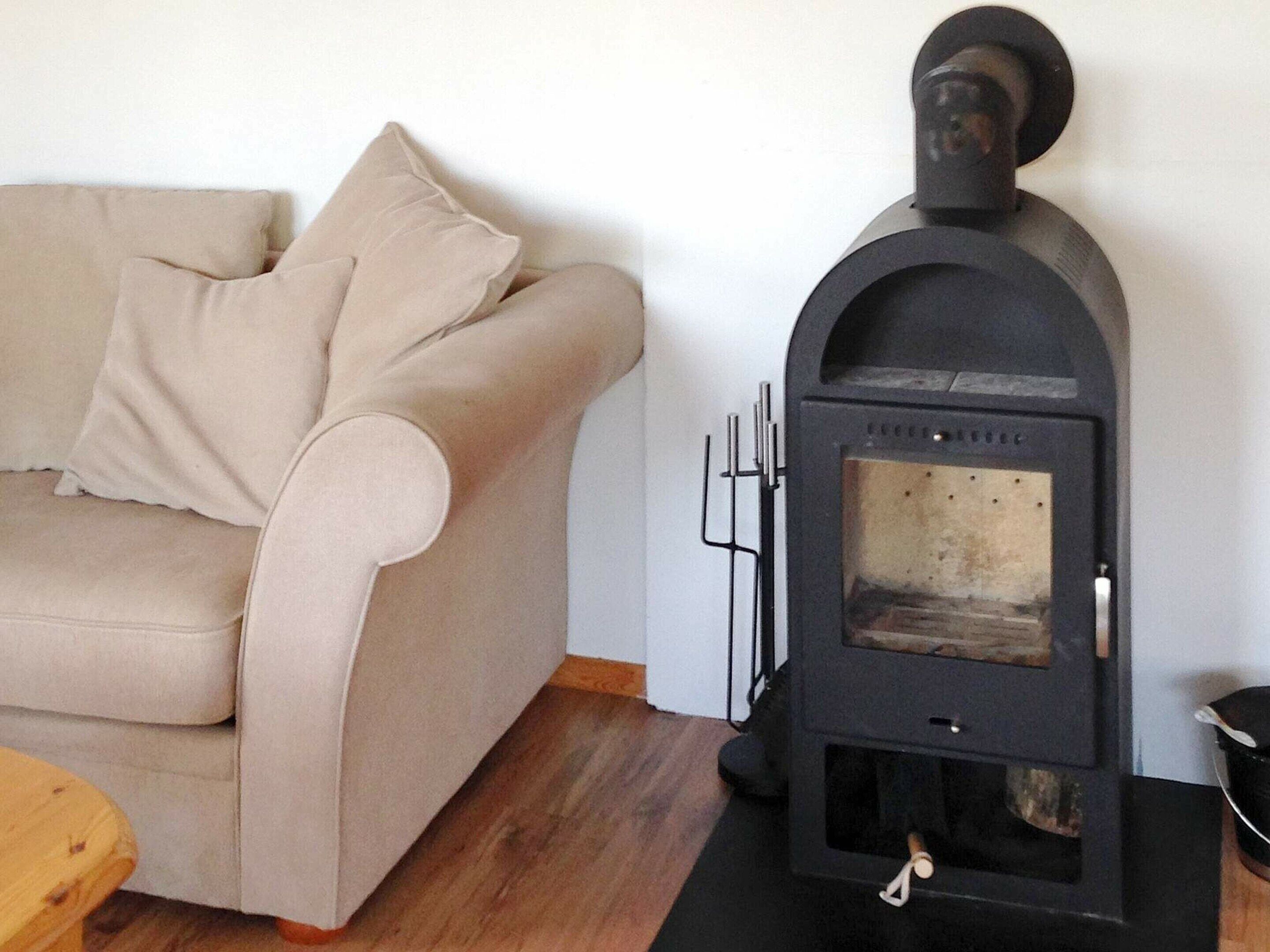 A beige sofa with a cushion, a black wood-burning stove, and a wooden table.
