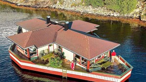 A houseboat with a covered deck, a dining area, and a small outdoor space with plants.