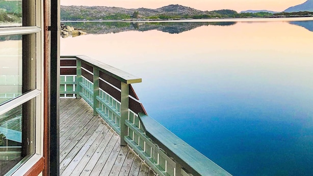 A wooden deck with a railing overlooking a calm lake with distant hills.