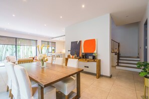 A modern living room with a wooden dining table, white sofas, and a kitchen area in the background.