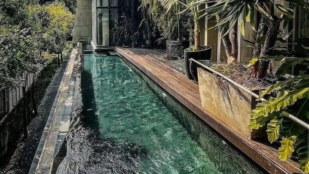 A swimming pool with a wooden deck, surrounded by lush greenery and a modern building. - The Oasis Tranquil Escape (Bangkok)