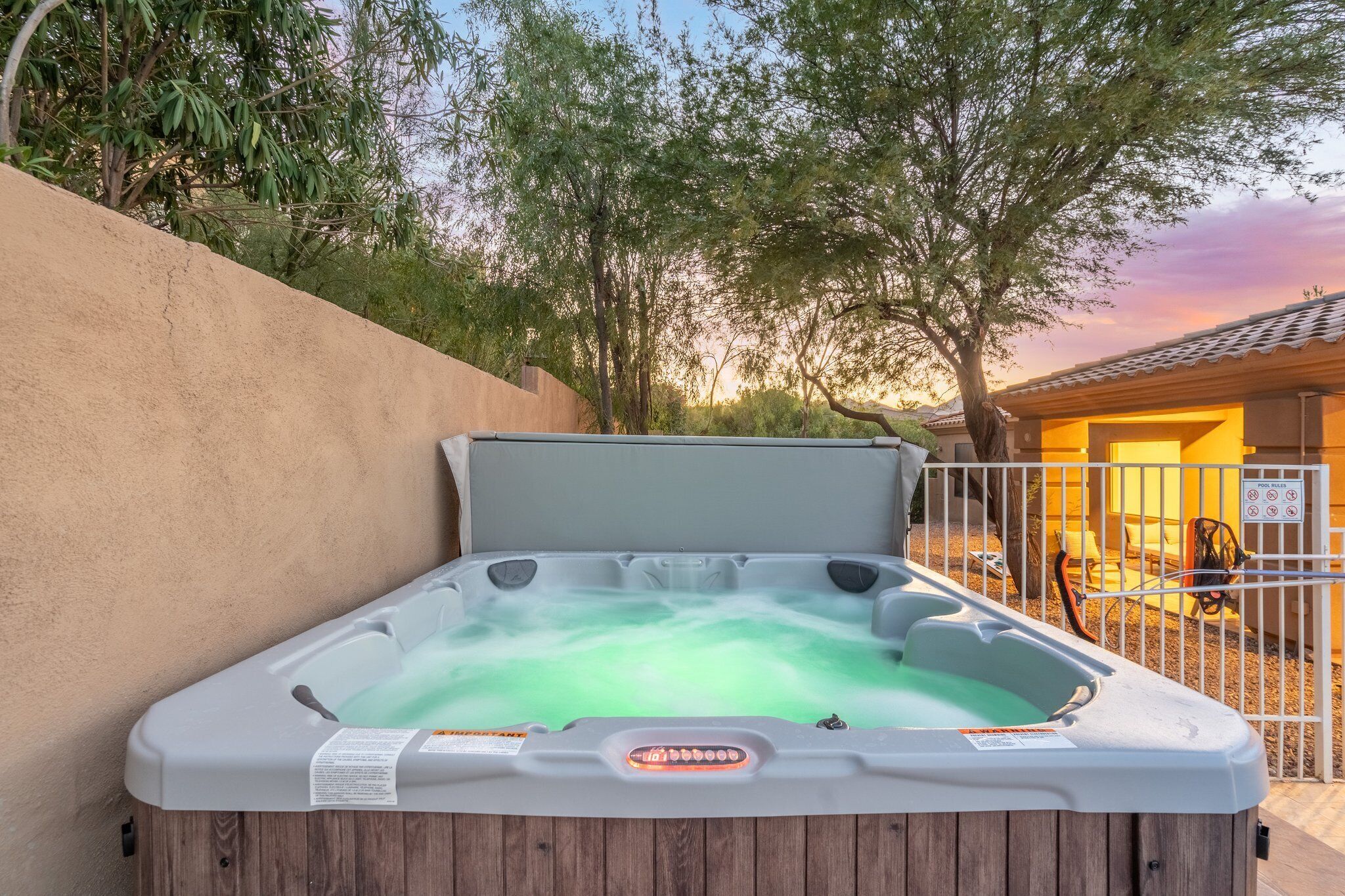 Een hottub met houten onderstel, omgeven door een beige muur en bomen.