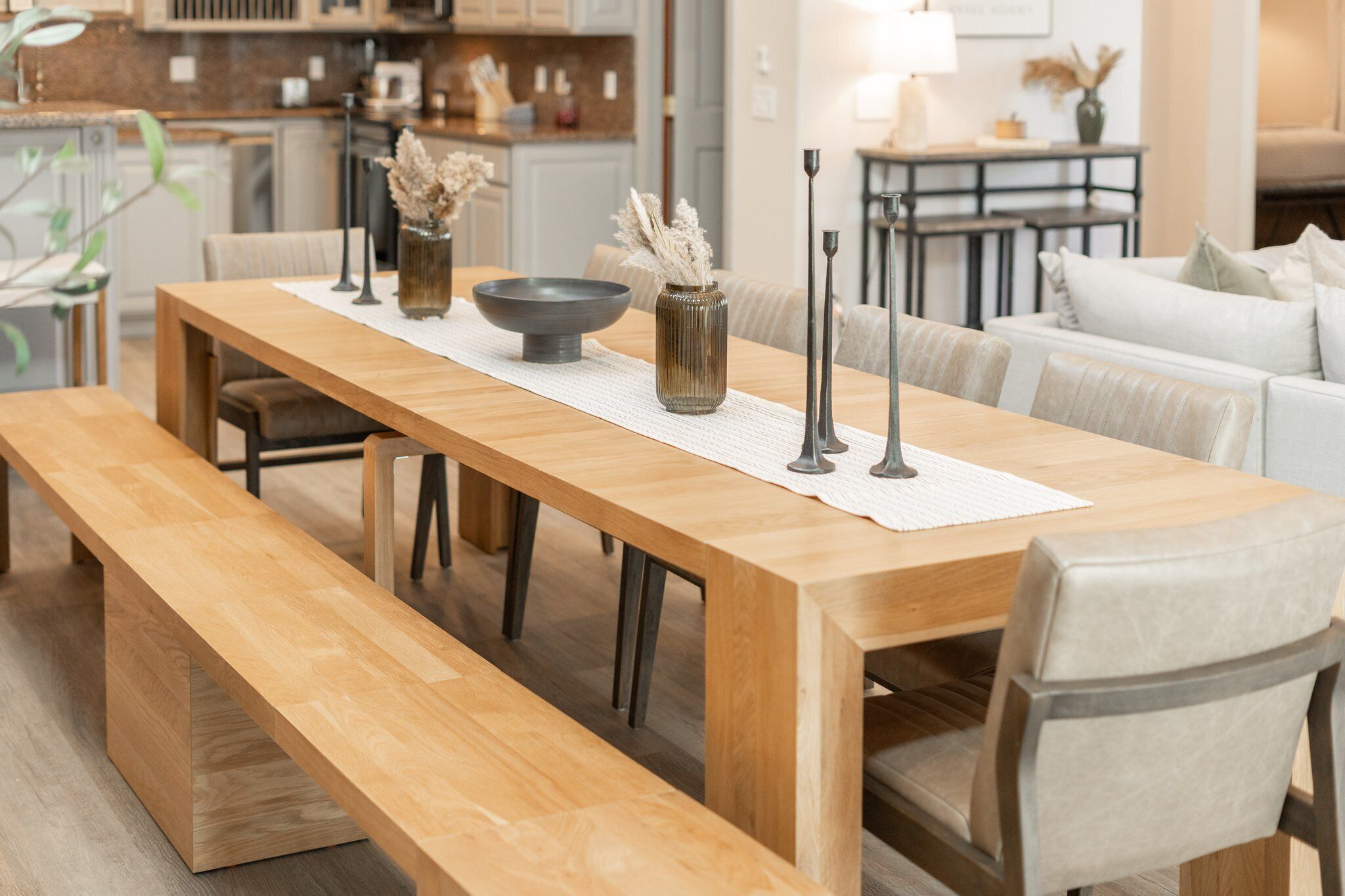 A wooden dining table with benches, a vase with dried flowers, and a bowl.