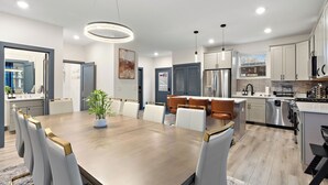 Una cocina moderna con electrodomésticos de acero inoxidable, un comedor con mesa y sillas de madera, y una sala de estar con sofá y planta.