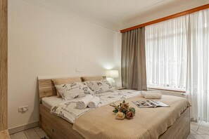 A neatly made bed with a patterned bedspread, a bedside lamp, and a window with curtains.