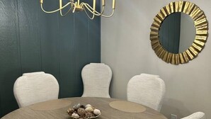 A dining room with a round table, six chairs, a chandelier, and a decorative mirror.