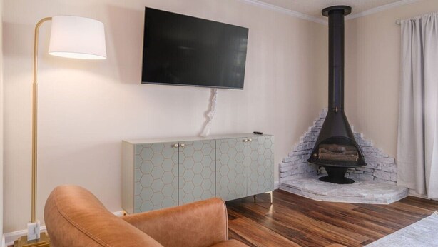 A living room with a sofa, a TV mounted on the wall, a cabinet, and a wood-burning stove.