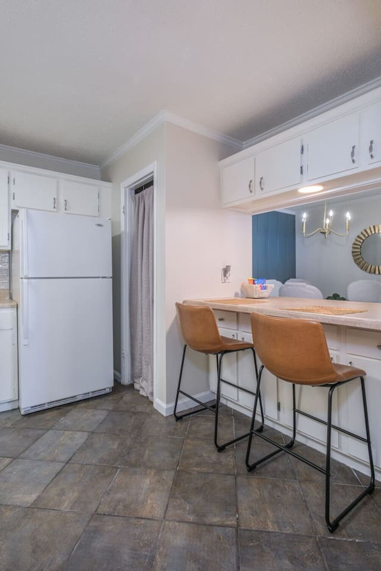 A compact kitchen with white cabinets, a double-door refrigerator, a dining table with two chairs, and a blue accent wall.
