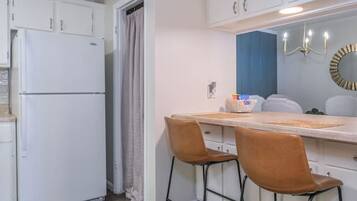 A compact kitchen with white cabinets, a double-door refrigerator, a dining table with two chairs, and a blue accent wall.