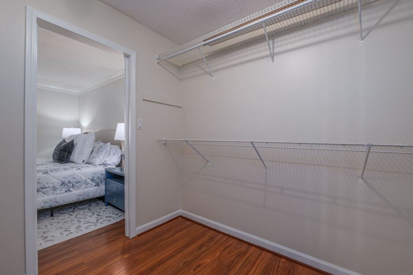 A bedroom with a bed, a nightstand, a lamp, and a closet with a wire shelf.