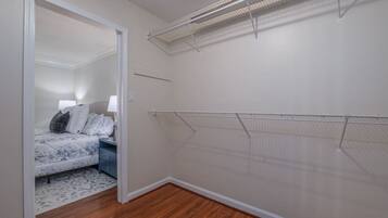 A bedroom with a bed, a nightstand, a lamp, and a closet with a wire shelf.