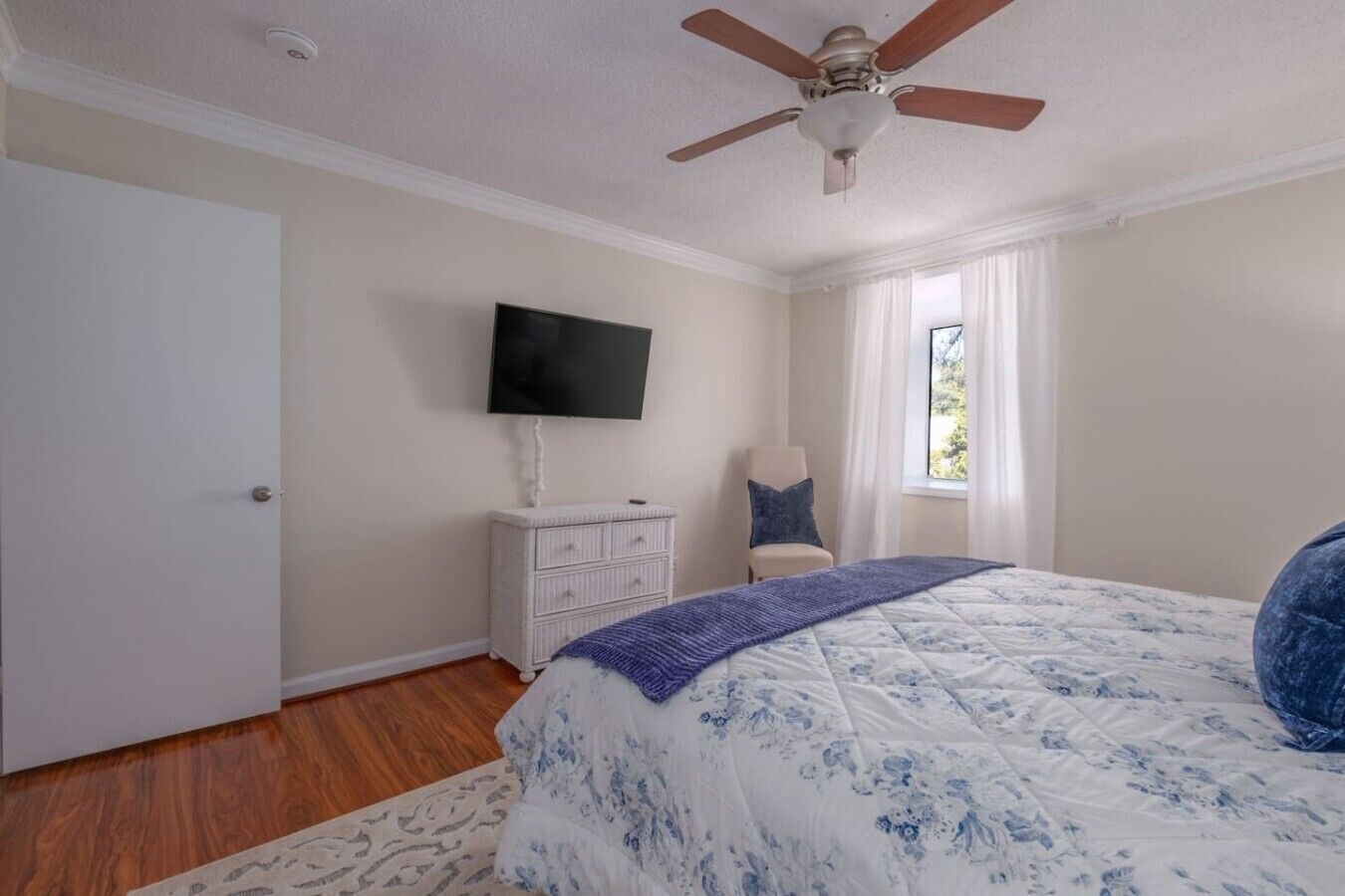 A bedroom with a bed, a dresser, a television, a ceiling fan, and a window.