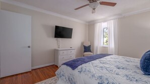 A bedroom with a bed, a dresser, a television, a ceiling fan, and a window.