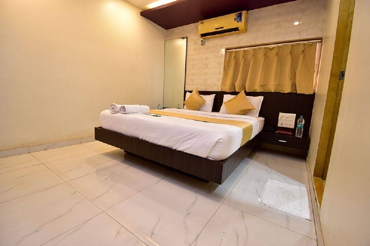 A modern hotel room with a large bed, a bedside table with a bottle, and a wall-mounted air conditioner.