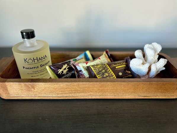 A wooden tray containing a bottle of Kohana Pineapple Daiquiri, Hawaiian chocolate bars, and a white sugar sculpture.