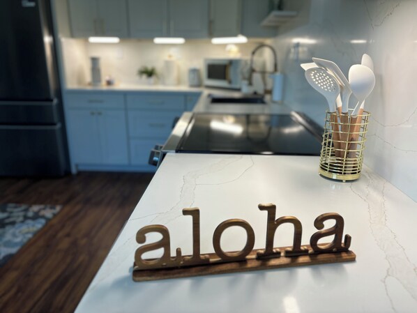 A kitchen counter with a marble top and a wooden sign spelling "aloha".