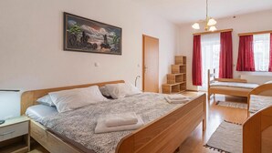 Ein Schlafzimmer mit Bett, Schreibtisch, Stuhl, Kleiderschrank, einem Fenster mit Vorhängen und einem Bild an der Wand.