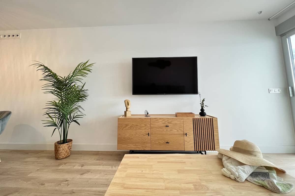 A modern living room with a wooden cabinet, a flat-screen TV, a large potted plant, and a woven basket.