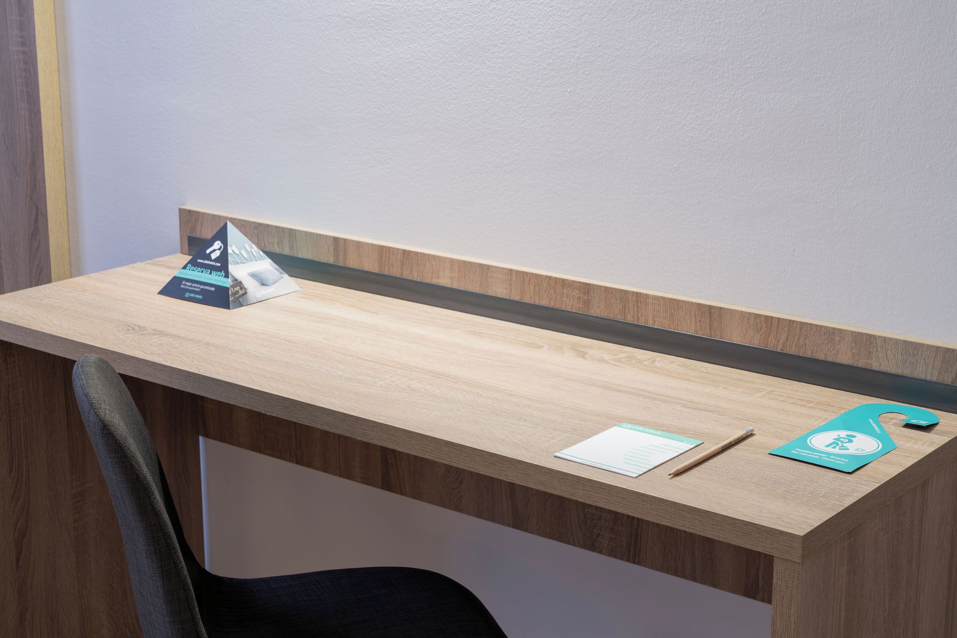 Un escritorio de madera con una división de vidrio, una silla y una pequeña mesa con un bolígrafo y una tarjeta.