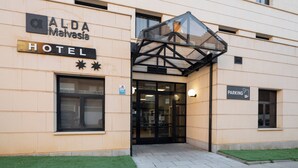 The exterior of ALDA Malasia Hotel with a glass entrance canopy, a sign indicating a parking area, and a small grassy area in front. - Alda Malvasia (Haro)