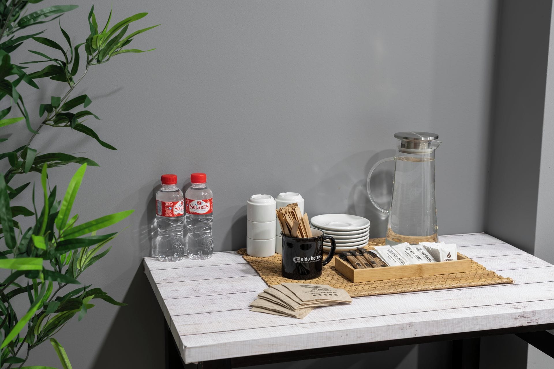 A table with water bottles, a coffee mug, a glass pitcher, and a box of napkins.