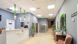 Un espace d’accueil avec un comptoir blanc, une pancarte indiquant une salle privée, un bureau de réception, un escalier et une horloge fixée au mur.