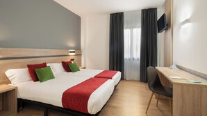 Une chambre d’hôtel comprenant un lit, deux tables de chevet, un bureau, une chaise et un téléviseur fixé au mur.