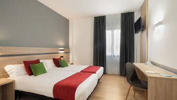 A hotel room with a bed, two bedside tables, a desk, a chair, and a TV mounted on the wall.