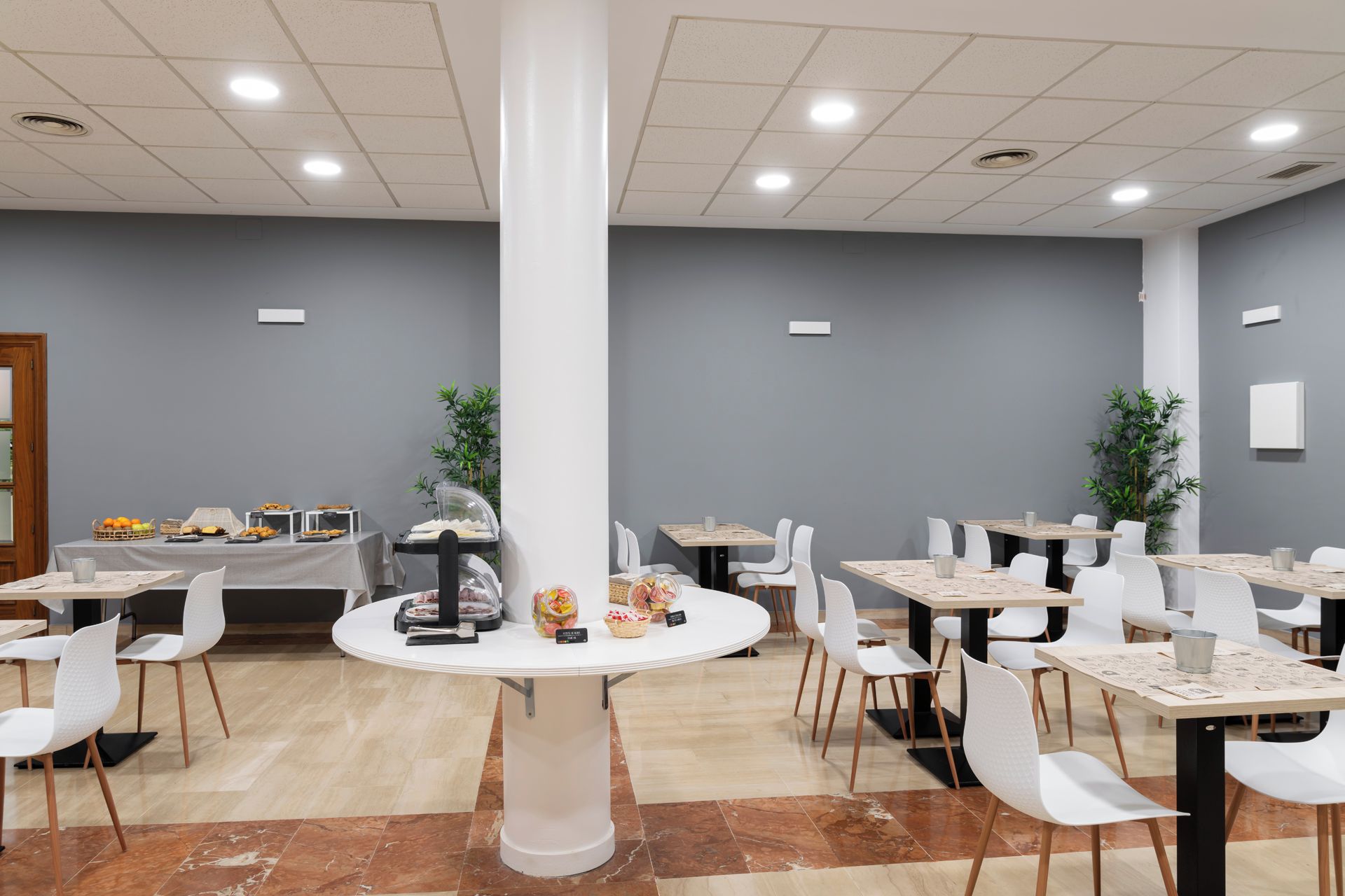 Un comedor moderno con mesas redondas, sillas blancas y una columna central.