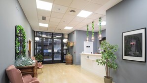 A reception area with a wooden reception desk, a pink chair, and a potted plant. - Alda Malvasia (Haro)